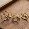Three gold-toned twisted ring earrings displayed on a dark wood tray over a neutral fabric background.