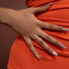 Close-up of a hand with a ring on an orange garment against a brown background