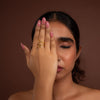 Woman with hand wearing a gold ring over face against a brown background