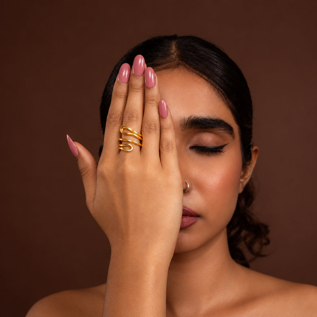 Woman with hand wearing a gold ring over face against a brown background
