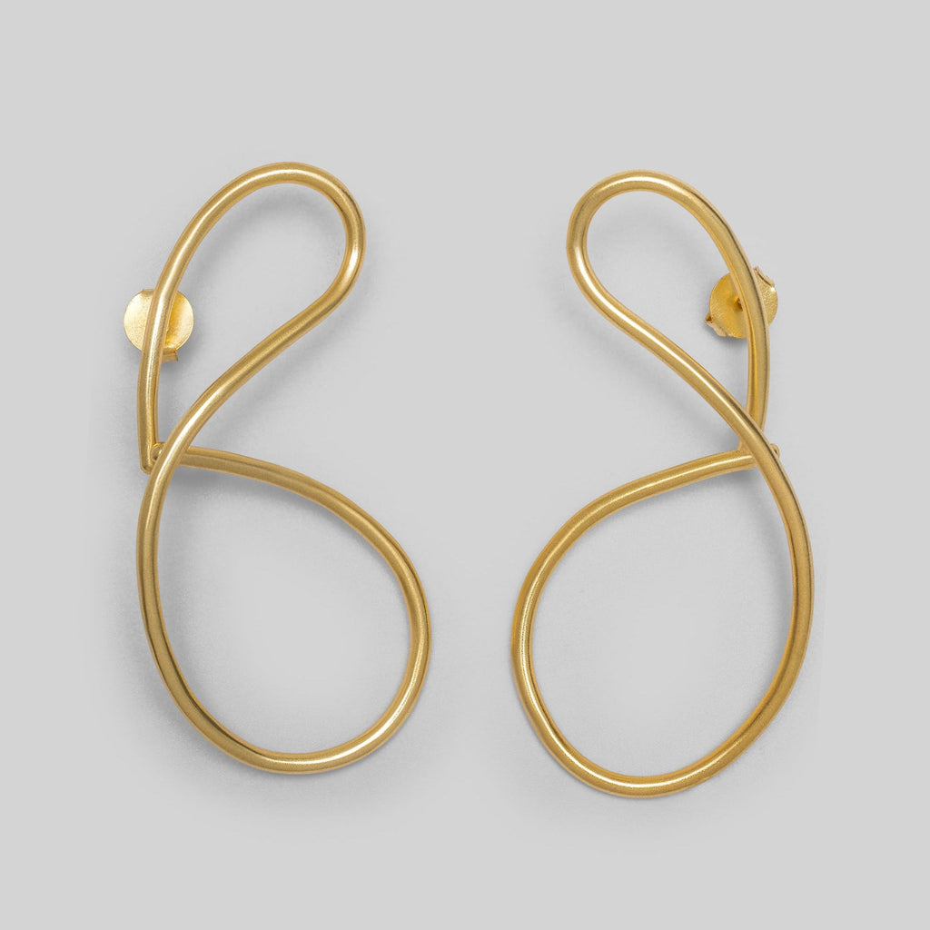 Gold statement earrings on a light gray background