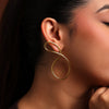 Close-up of a woman wearing a gold infinity-shaped earring against a warm-toned background.