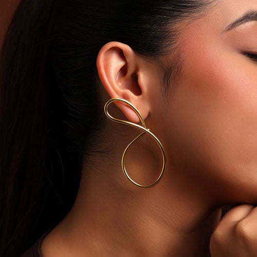 Close-up of a woman wearing a gold infinity-shaped earring against a warm-toned background.