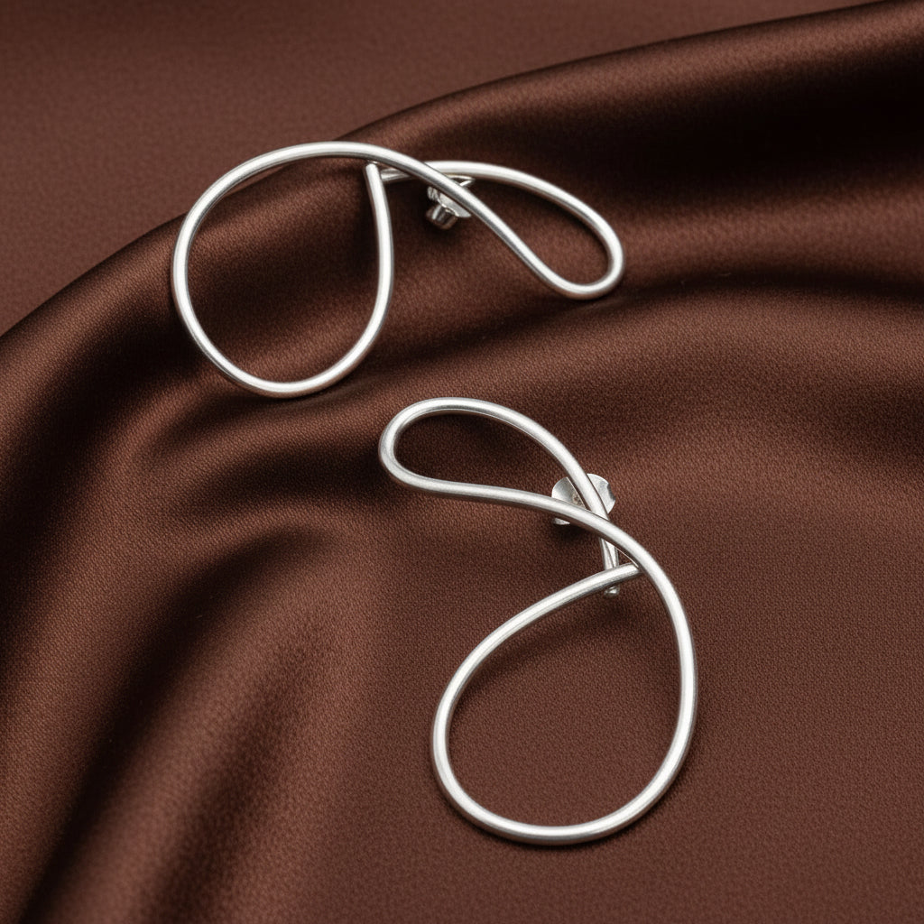 Pair of silver earrings on a brown shimmery cloth