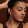 Woman wearing a silver statement earring against a brown background