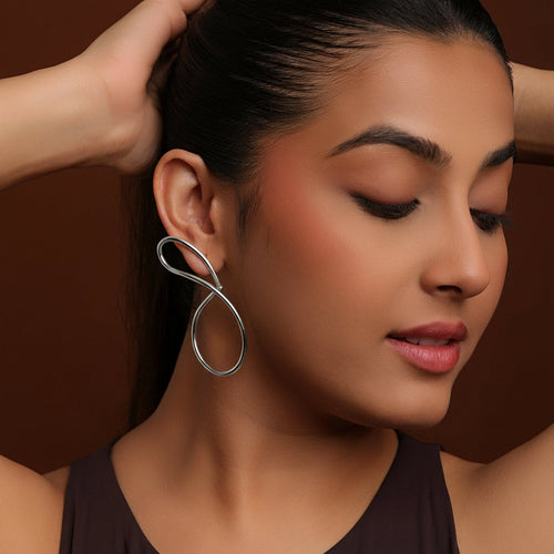 Woman wearing a silver statement earring against a brown background