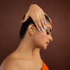 Woman in an orange dress, gold earcuff with a brown background
