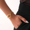 Gold infinity bracelet on a wrist with a neutral background