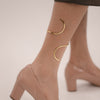 Beige high-heeled shoes worn with gold anklets on a neutral background