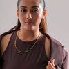 Woman wearing a brown top and gold necklace against a plain background