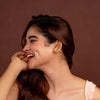 Woman in a pink dress and gold earcuffs posing against a brown background