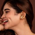 Woman in a gold earcuffs posing against a brown background