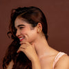 Woman in a pink dress and gold earcuffs posing against a brown background