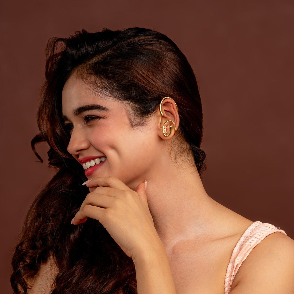 Woman in a pink dress and gold earcuffs posing against a brown background