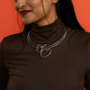 Woman wearing a brown turtleneck and silver necklace against an orange background
