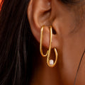 Gold hoop earring with a pearl accent worn by a person against an orange background