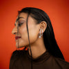Woman wearing silver hoop earrings against a red background