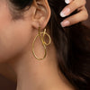Gold dangling earrings worn by a women with a neutral background