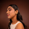 Woman wearing gold hoop earrings against a brown background