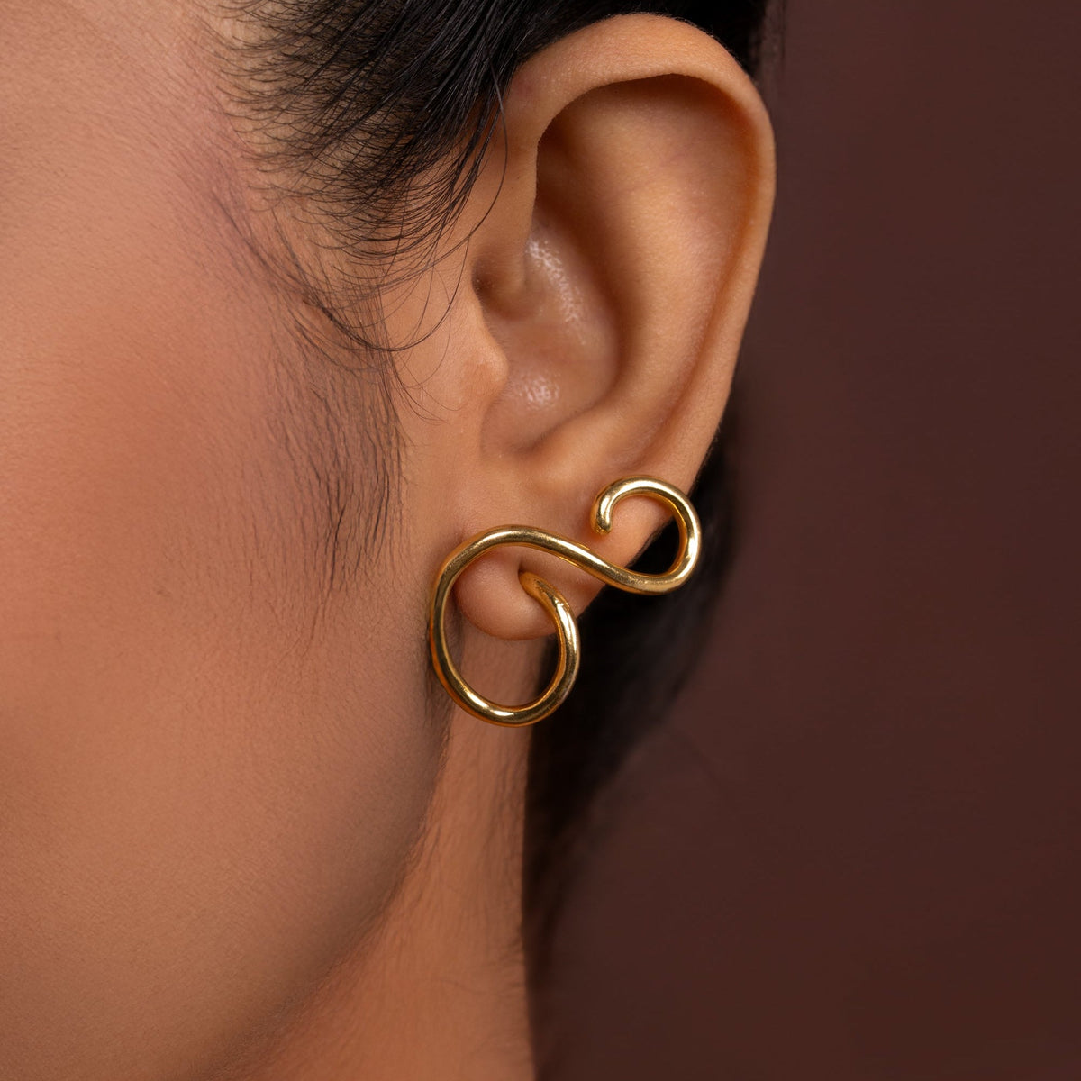 Gold ear cuff worn by a person on a brown background