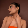 Woman wearing an orange dress and gold earrings against a brown background
