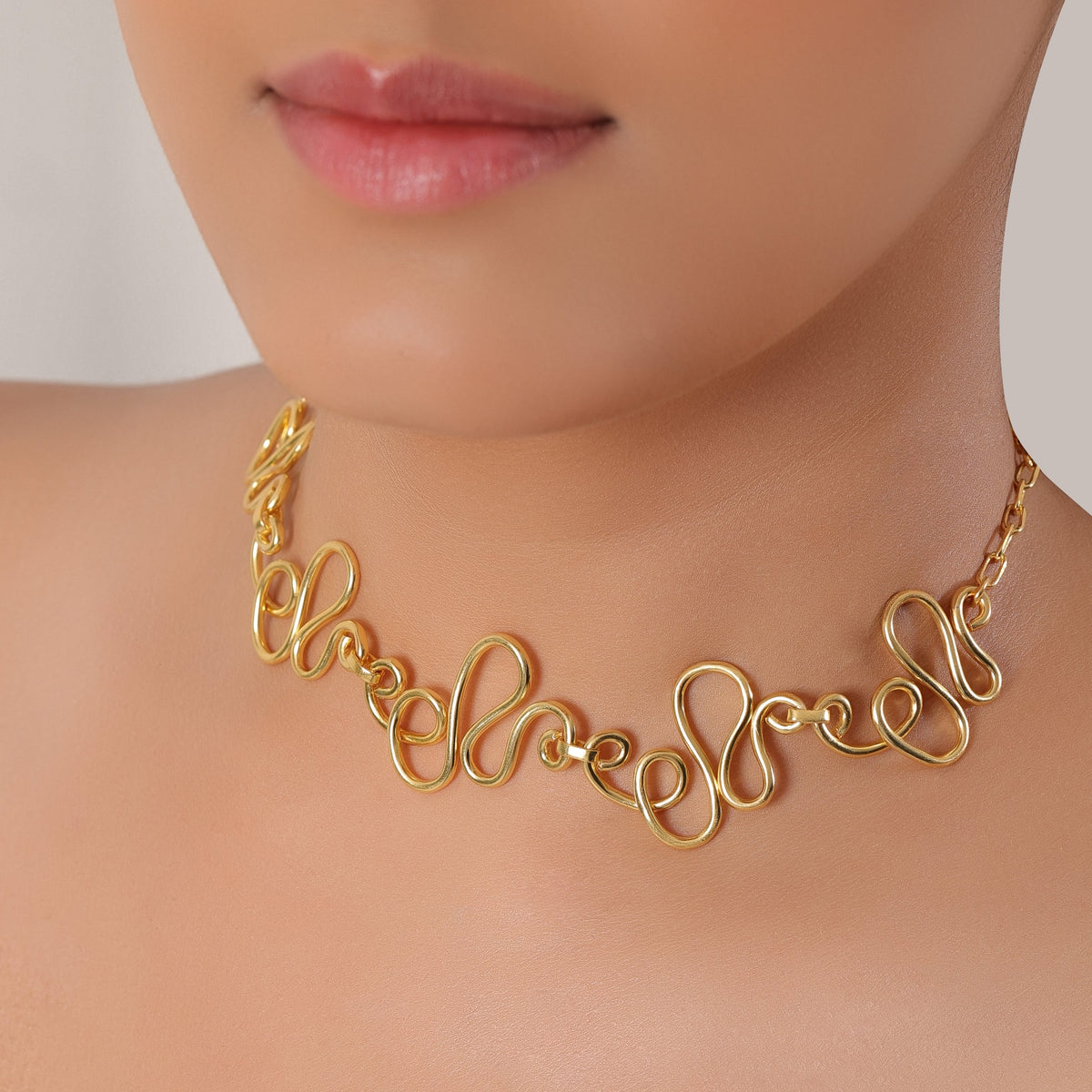 Gold choker necklace with cursive design on a neutral background