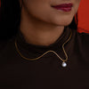 Close-up of a pearl necklace on a person wearing a black turtleneck with a red background.