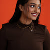 Woman wearing a brown top and gold necklace with baroque pearl against an orange background