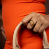 Hand holding a beige handbag with a gold ring on an orange background