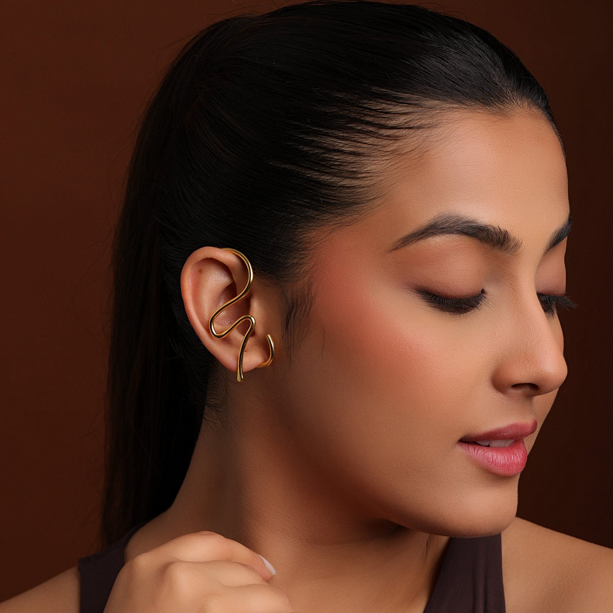 Woman wearing a gold earcuff against a brown background