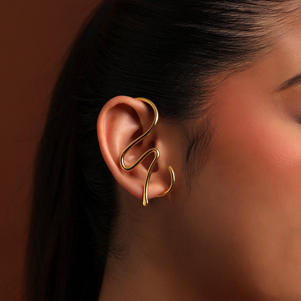 Gold ear cuff worn by a person against a brown background