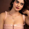 Woman wearing a pink dress with a gold necklace against a brown background