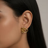 Gold earring worn by a person with dark hair against a neutral background