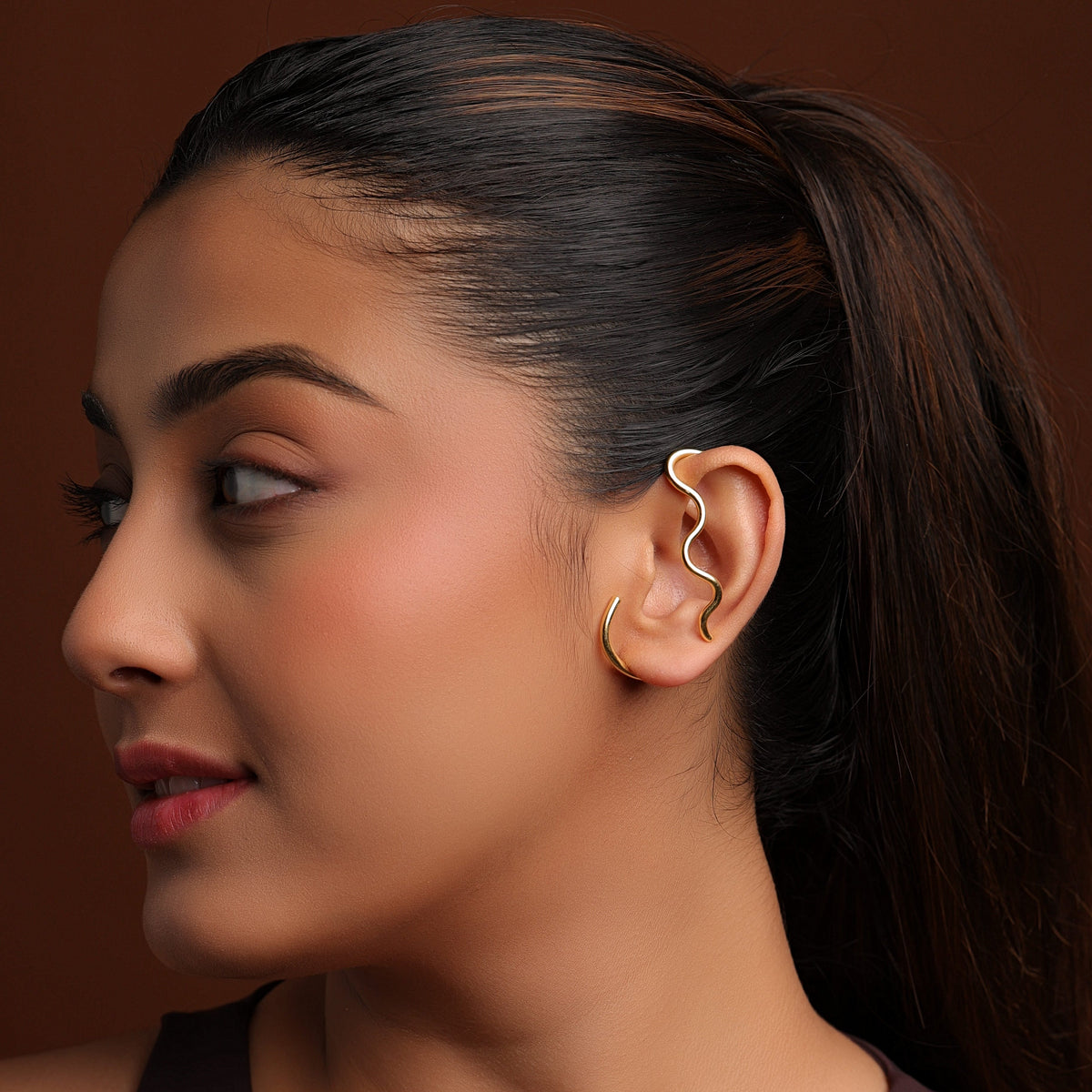 Woman wearing a unique ear cuff against a brown background