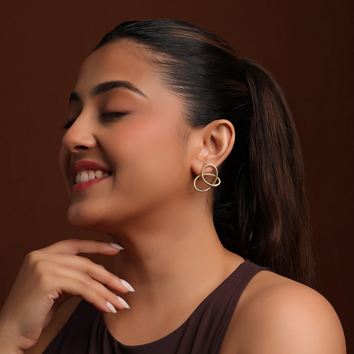Woman wearing gold earrings against a brown background