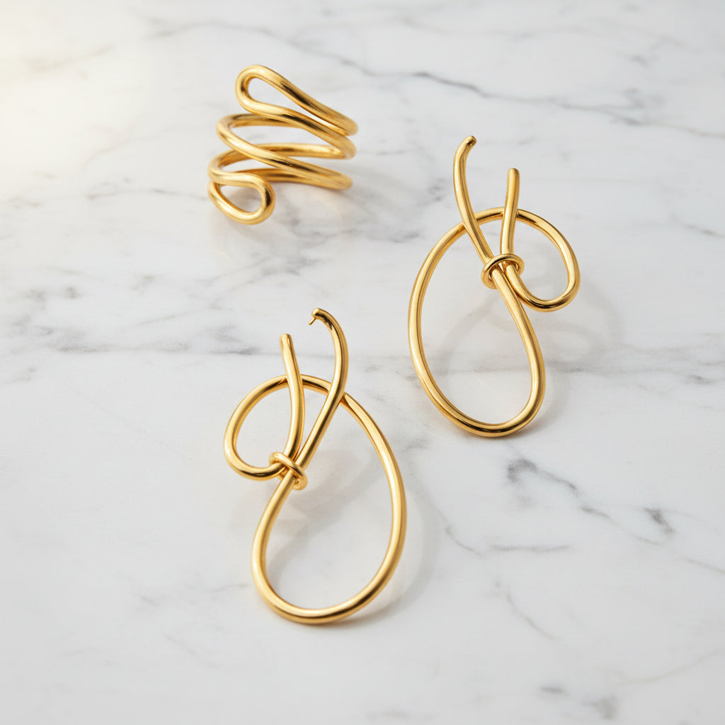 Gold wire-shaped earrings and a ring on a dark reflective surface