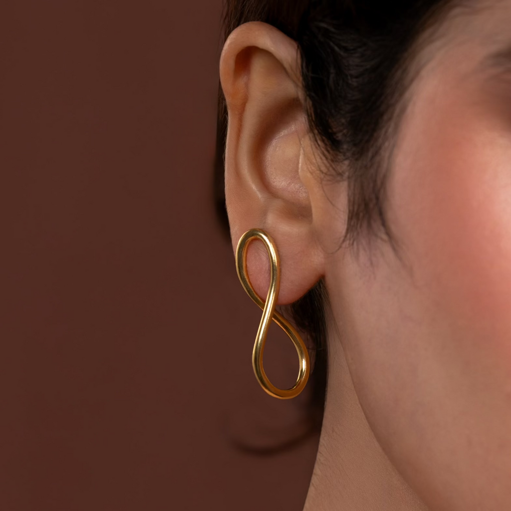 Gold infinity-shaped earring worn on an ear with a brown background