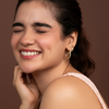 Woman with a smile wearing a gold earring against a brown background