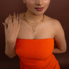 Woman wearing an orange strapless dress and gold necklace with a unique design against a brown background