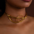 Gold choker necklace worn by a person with a brown background