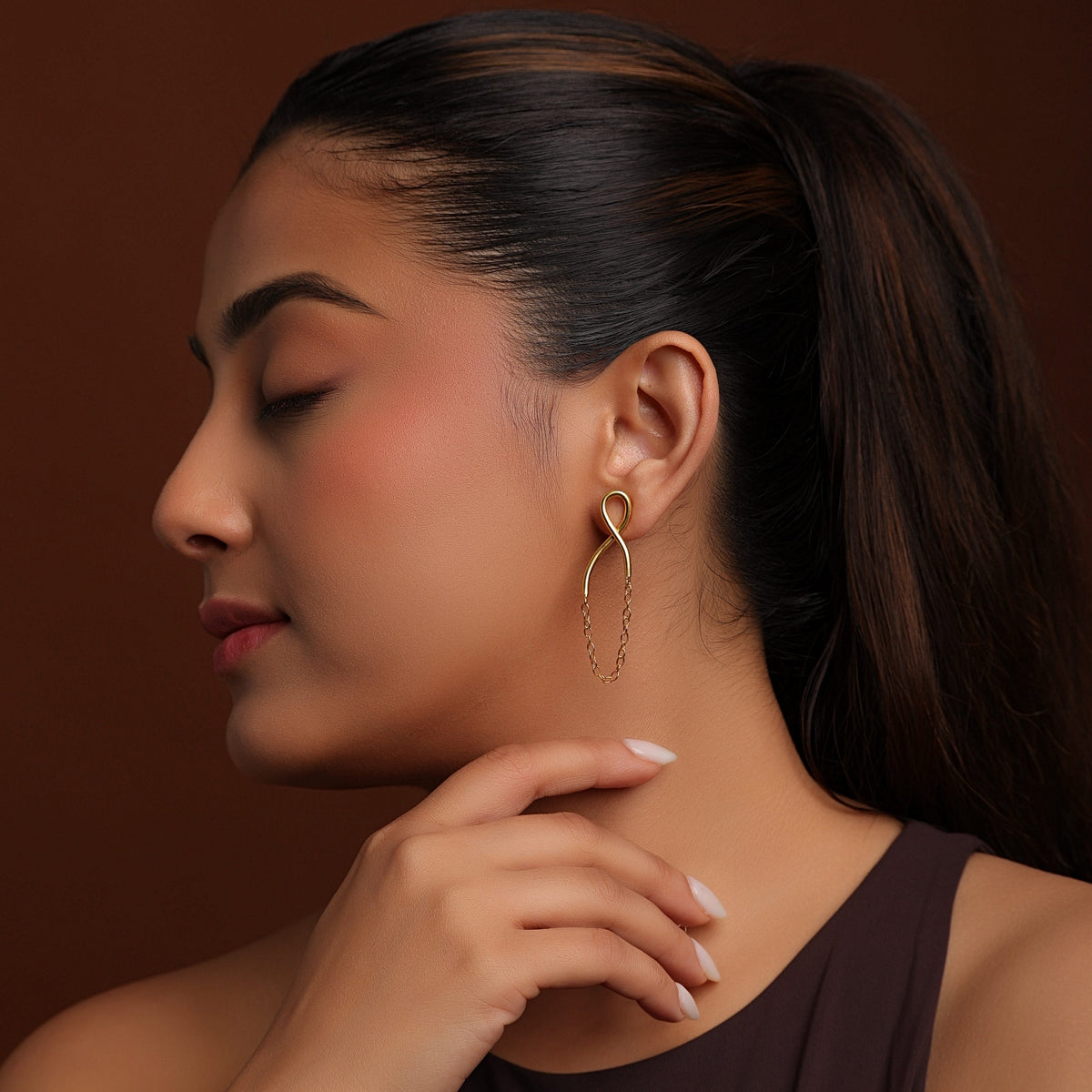 Woman wearing a gold earring against a brown background