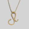 Gold necklace with a unique shaped pendant on a gray background