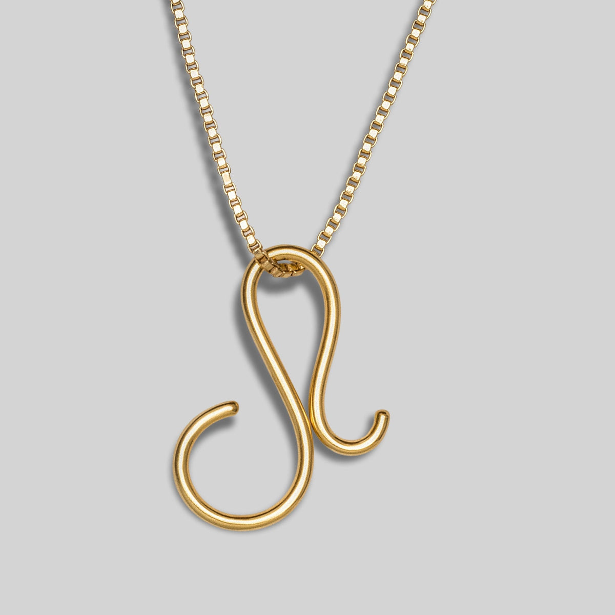 Gold necklace with a unique shaped pendant on a gray background