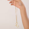 Hand holding a gold necklace with a unique pendant against a light background