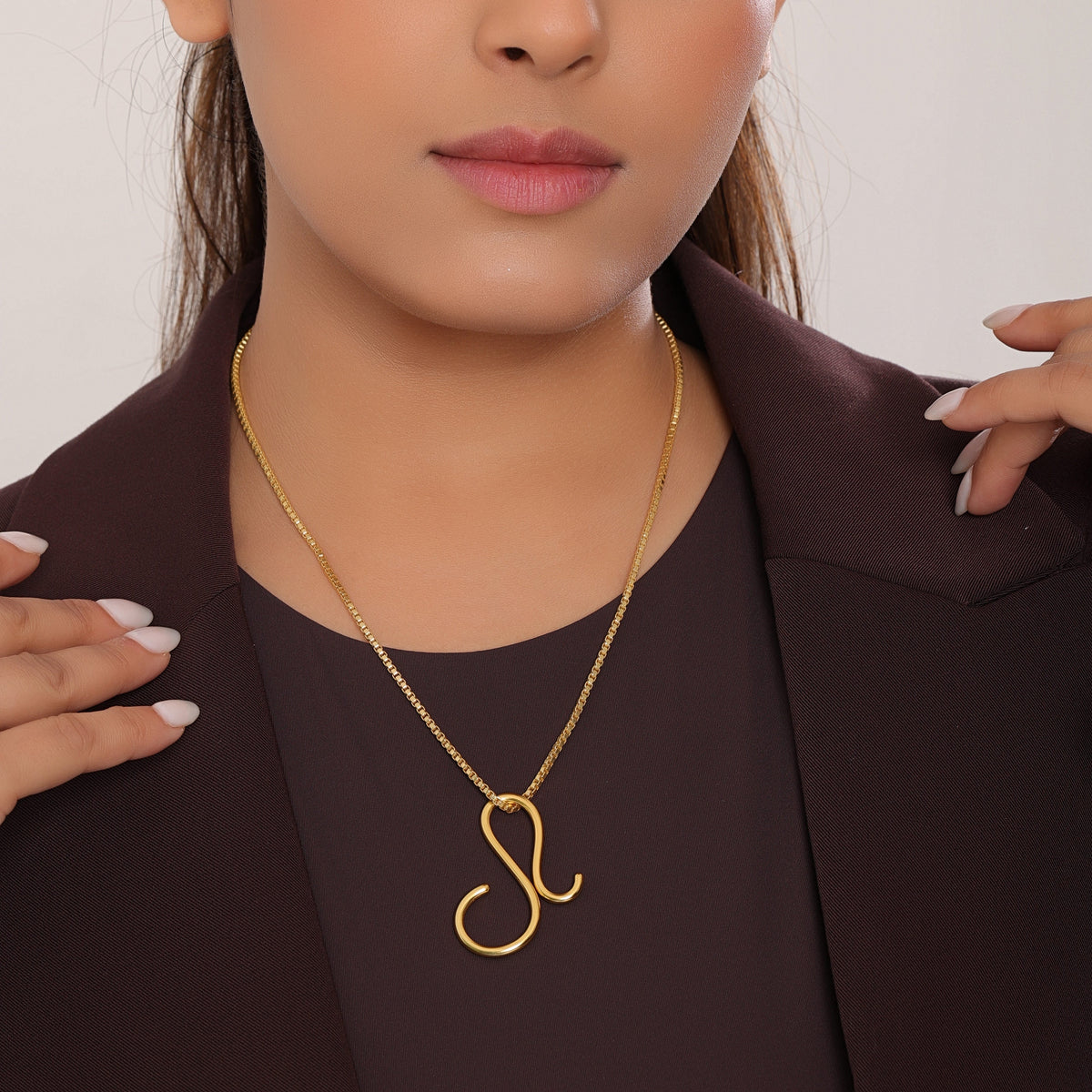 Woman wearing a gold necklace with a pendant against a neutral background