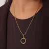 Gold necklace with a unique pendant on a model wearing a dark brown outfit.