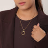 Woman wearing a gold necklace with a circular pendant against a neutral background