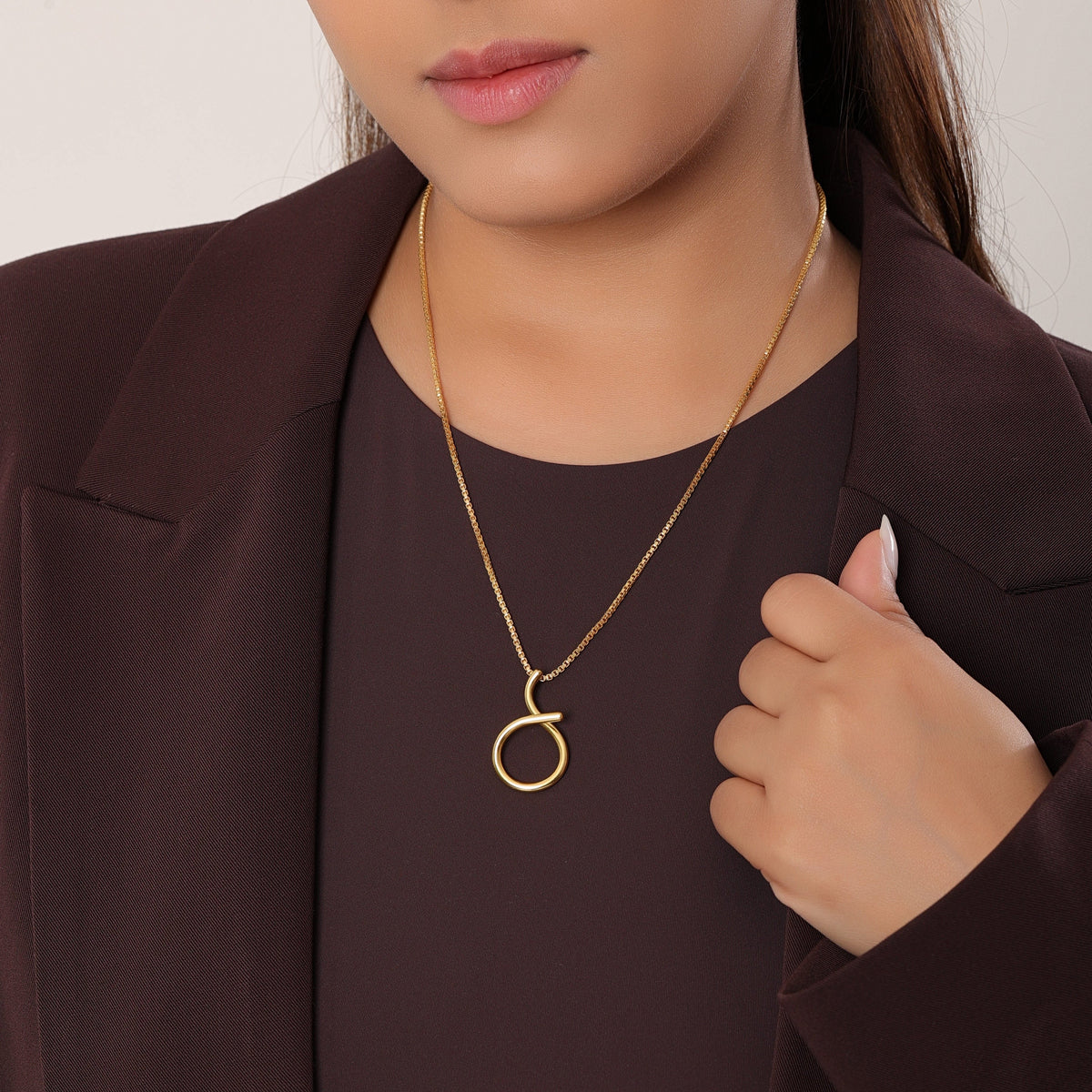 Woman wearing a gold necklace with a circular pendant against a neutral background