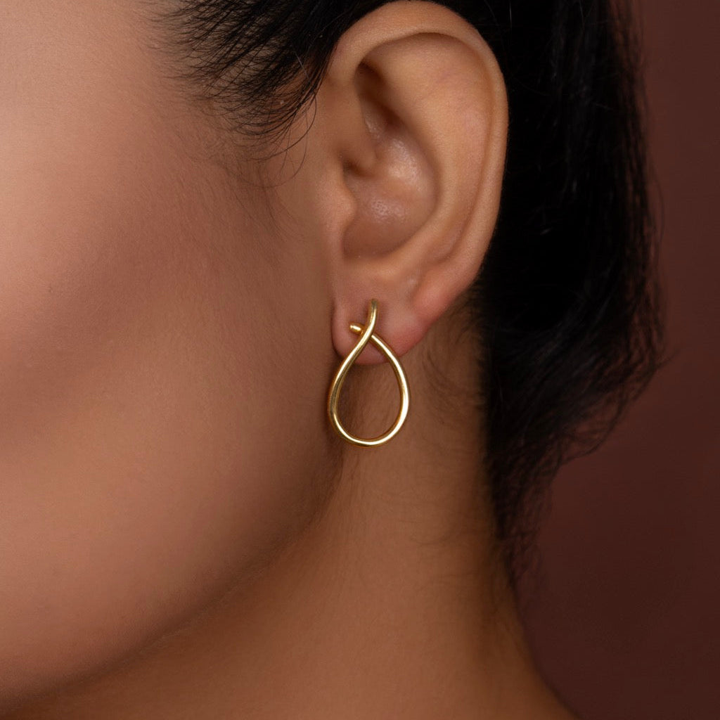Gold tiny earring worn by a person against a neutral background