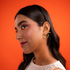 Woman wearing gold earrings against an orange background